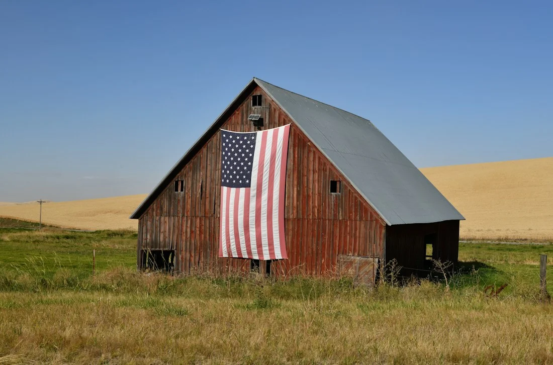 Weathered red barn displaying an American flag amid open farmland in eastern Washington.